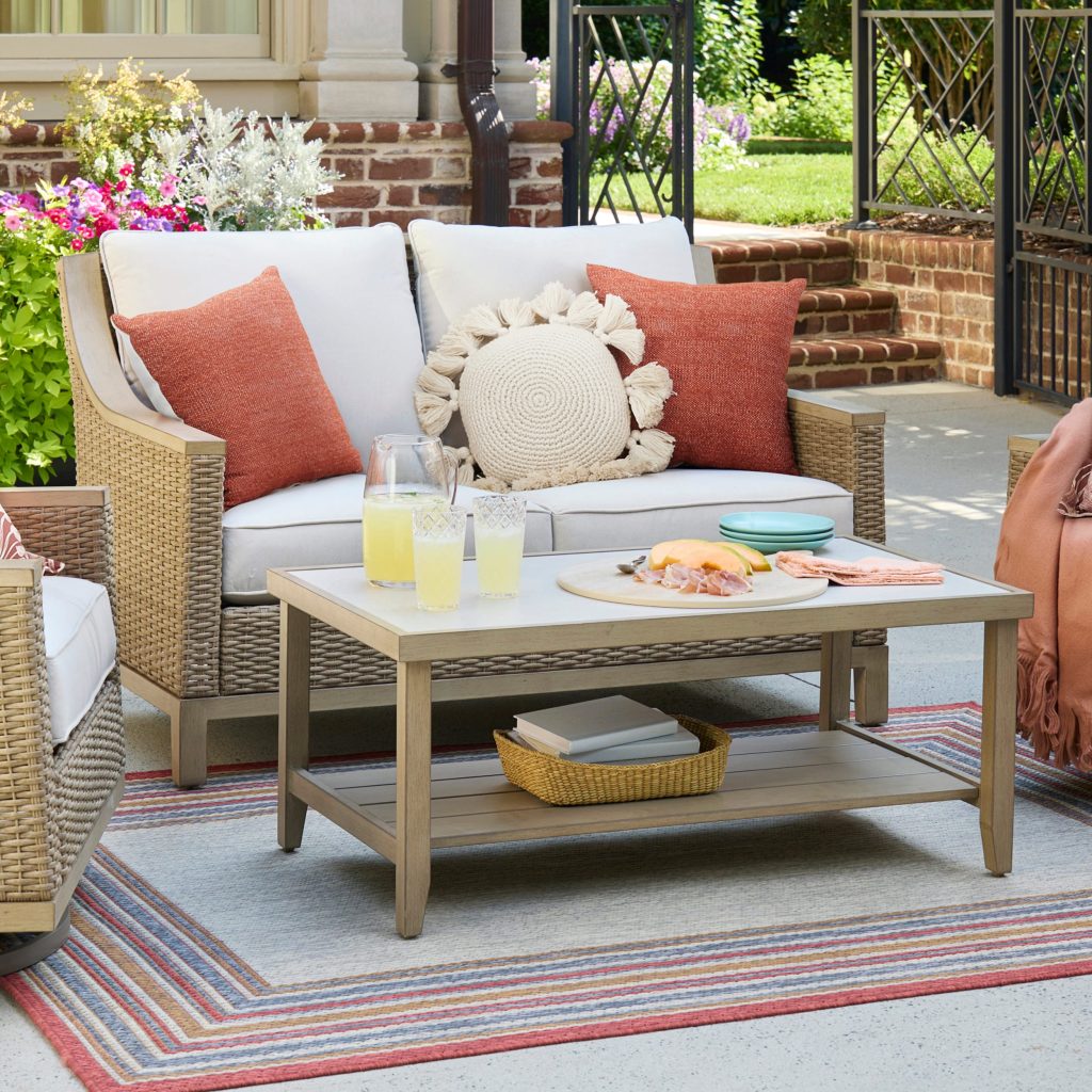 Allen + Roth Rosedale wicker loveseat with off-white cushions next to a sintered stone top table